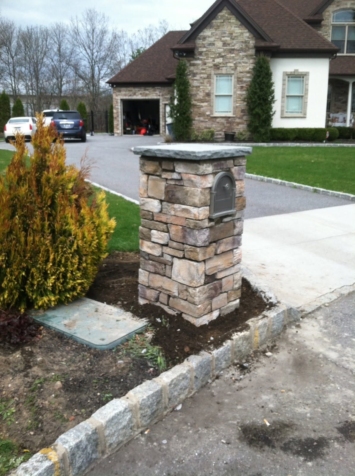 Stone masonry mailbox pillar with a bluestone cap beside a residential driveway