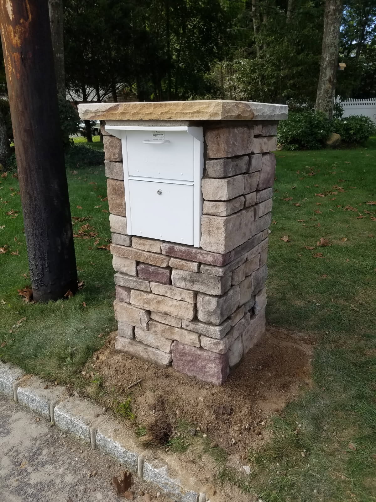 Stone masonry pillar with an integrated white package mailbox and natural stone cap
