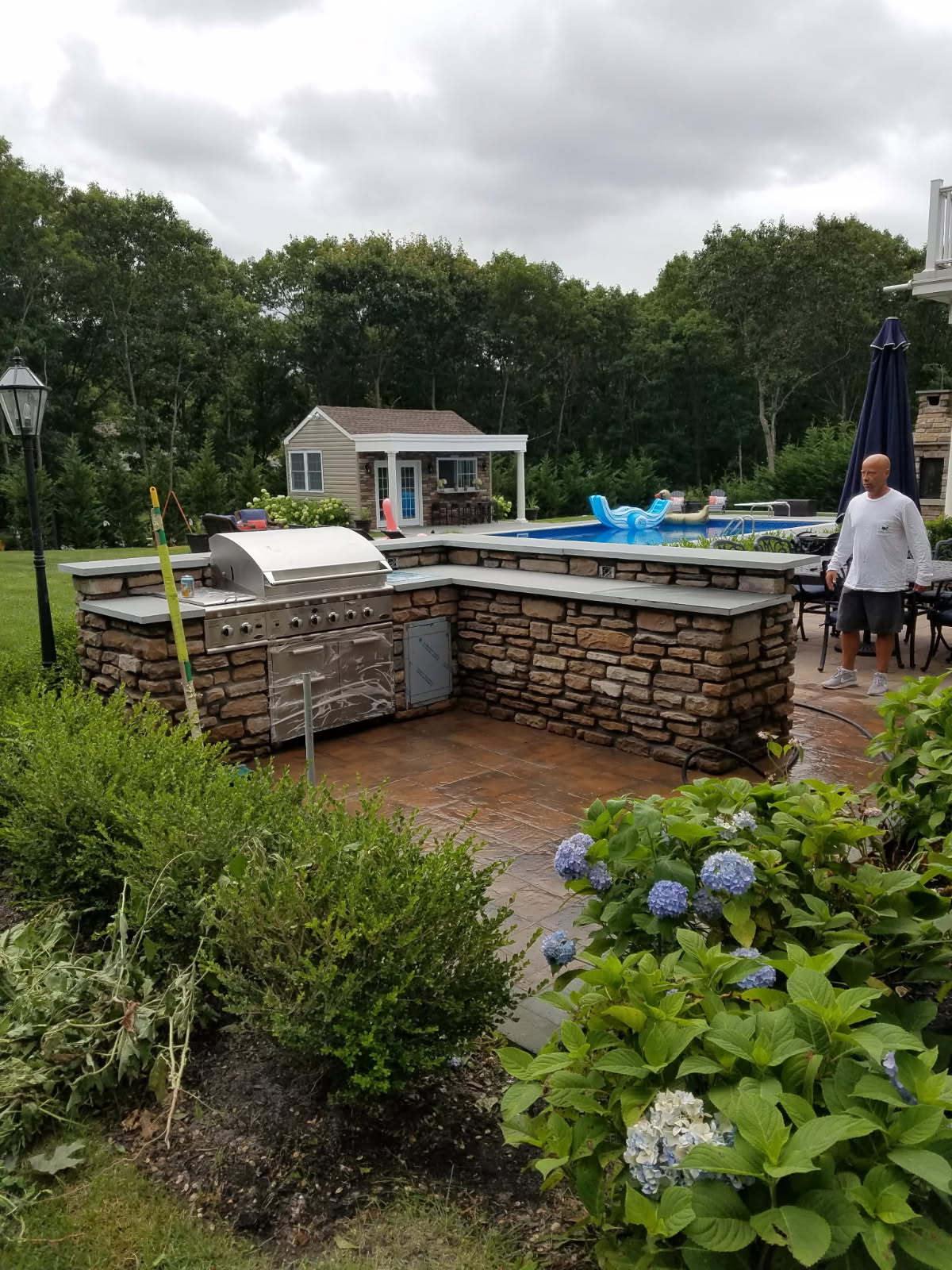 Stone veneer outdoor kitchen with built-in stainless steel grill beside a pool