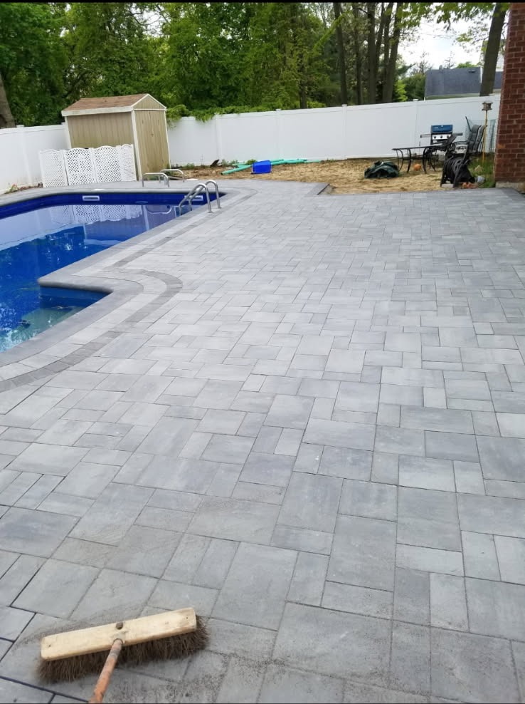 New gray interlocking paver deck installed around a backyard swimming pool